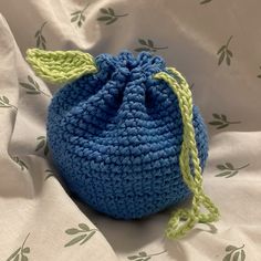 a crocheted blue bag sitting on top of a white bed sheet with green leaves