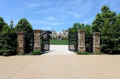 an entrance to a large home with stone pillars and gates leading into the driveway area