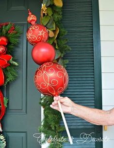 a person holding two red christmas balls in front of a green door with wreaths on it