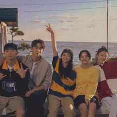 a group of young people sitting next to each other on a bench near the ocean