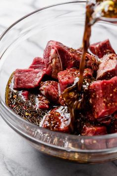 a bowl filled with meat and seasoning being poured into it to make steak sauce