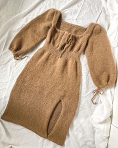 a brown sweater dress laying on top of a bed next to a white sheet and pillow