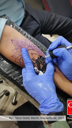 a person getting a tattoo done on his arm with blue gloves and a pen in their hand