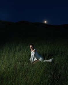 a woman sitting in tall grass at night