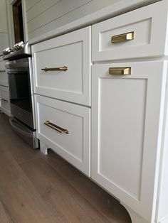 the kitchen cabinets are all white and have brass pulls on them to match the wood flooring