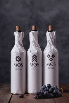 three wine bottles sitting on top of a wooden table next to some grapes and blueberries