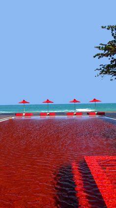 an empty beach with red umbrellas and blue water