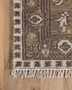 a brown and white rug with fringes on top of a wooden floor next to a wall