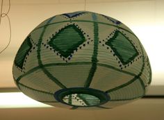 a green and white paper lantern hanging from the ceiling in front of a light fixture