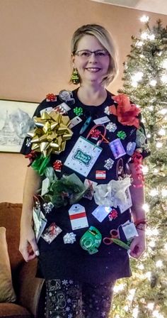 a woman standing in front of a christmas tree with gifts on her shirt and tie