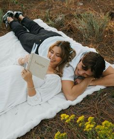 a man and woman laying on a blanket reading a book