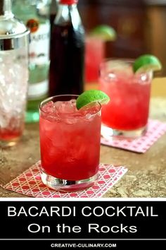 two cocktails with lime garnish sit on napkins next to liquor bottles