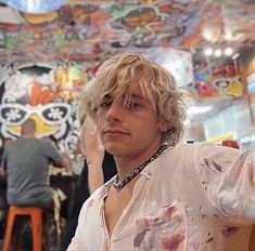 a young man with blonde hair sitting at a table in front of a colorful wall