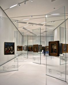 an art gallery filled with paintings and people looking at them in glass cases on the wall