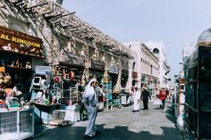 several people walking down the street in front of some shops and buildings with many items on display