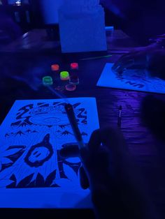 a person is drawing on a piece of paper with neon lights in the dark room