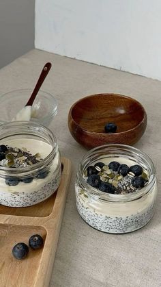 two jars filled with yogurt and blueberries on top of a wooden cutting board