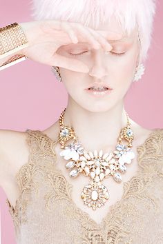 a woman with white hair is holding her hand up to her face while wearing a necklace and earrings