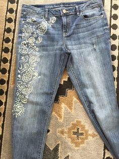 a pair of jeans that are sitting on top of a rug with an embroidered design