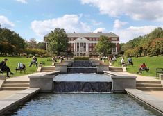 people sitting on benches around a fountain in the middle of a grassy area with trees