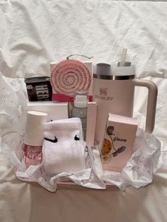 a basket filled with personal care items on top of a white sheet covered bed next to a cup