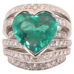 an emerald and diamond heart shaped ring with two rows of diamonds around the band, set in 18k white gold