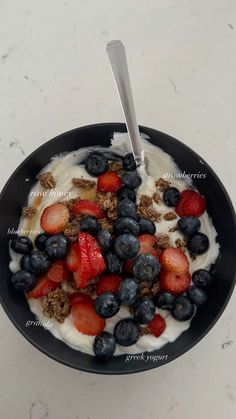 yogurt with berries and granola in a black bowl on a white counter