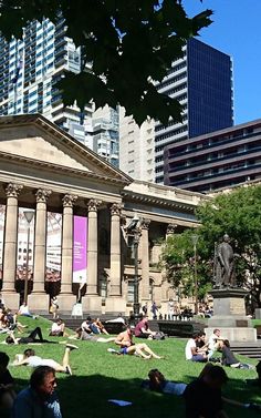 many people are laying on the grass in front of an old building with columns and pillars