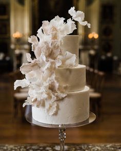 a three tiered cake with white flowers on the top is sitting on a table