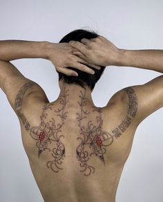 the back of a man with tattoos on his upper and lower body, holding his hands behind his head