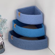 three crocheted pet beds stacked on top of each other next to a vase with flowers