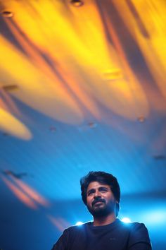 a man standing in front of a blue and yellow ceiling with lights shining down on him