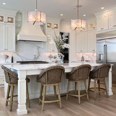 a large kitchen with white cabinets and marble counter tops, two bar stools at the center