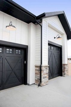 two black garage doors on the side of a white house with brick pillars and windows