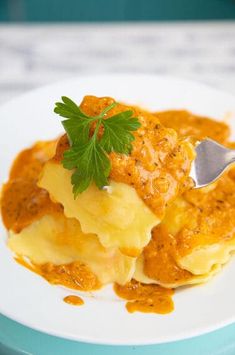 a white plate topped with ravioli covered in sauce and garnished with parsley