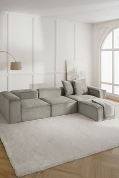 a living room with a large sectional couch and white rugs on the hardwood floor