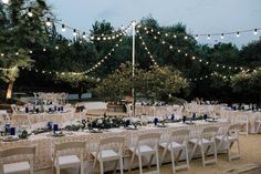 tables and chairs are set up for an outdoor wedding reception with string lights strung over them