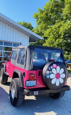 a pink and black jeep parked in front of a building with a flower painted on the side