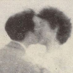 an old black and white photo of two people kissing each other in front of a window