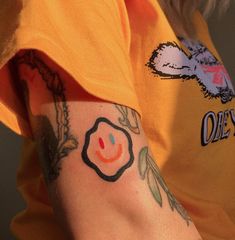 a person with a smiley face tattoo on their left arm and right arm is wearing an orange t - shirt