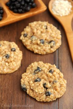 three oatmeal breakfast cookies with blueberries on a wooden table next to two spoons