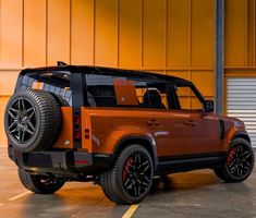 an orange and black suv parked in a parking lot next to a garage door with yellow walls