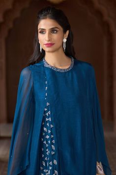 Teal blue overlapped tunic with contrasting geometric pattern hand embroidery and cascading draped cape sleeves. - Aza Fashions Designer Blue Tops With Mirror Work, Blue Tops With Mirror Work, Designer Blue Top With Traditional Drape, Elegant Blue Tops With Traditional Drape, Blue Anarkali Set With Cape Sleeves, Blue Dress With Sheer Dupatta And Cape Sleeves, Blue Designer Dress With Cape Sleeves, Blue Sets With Sheer Dupatta And Cape Sleeves, Blue Fusion Style Dupatta With Traditional Drape