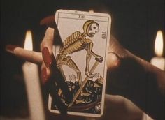 a skeleton tarot card being held in front of candles with the image of a person holding it