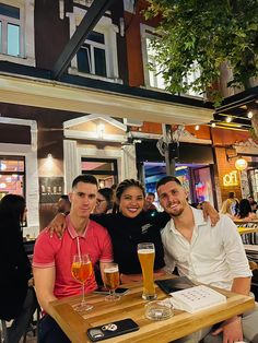 three people sitting at a table with beers in front of them