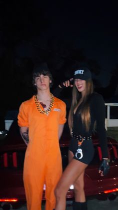 two people dressed in costumes standing next to a red car at night with one person wearing an orange jumpsuit