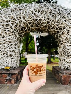 a person holding up a cup with a straw in front of an arch shaped sculpture