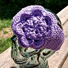 a purple crocheted hat sitting on top of a glass headpiece in front of a wooden bench