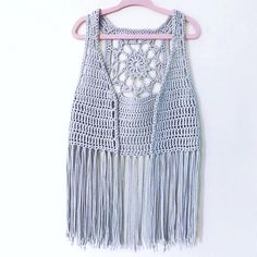 a crocheted top hanging on a hanger with tassels and beads