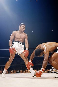 two men in shorts and red boxing gloves stand on one foot as another man kneels down